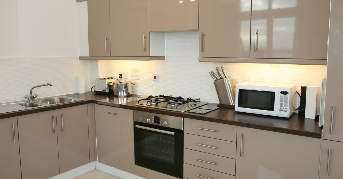 A modern kitchen with taupe cabinets, stained wood countertops, an oven, and a microwave lying on the counter.