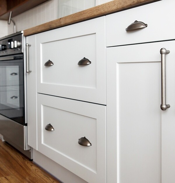 White kitchen cabinets with silver hardware and wooden countertops. The kitchen features an oven and a microwave.