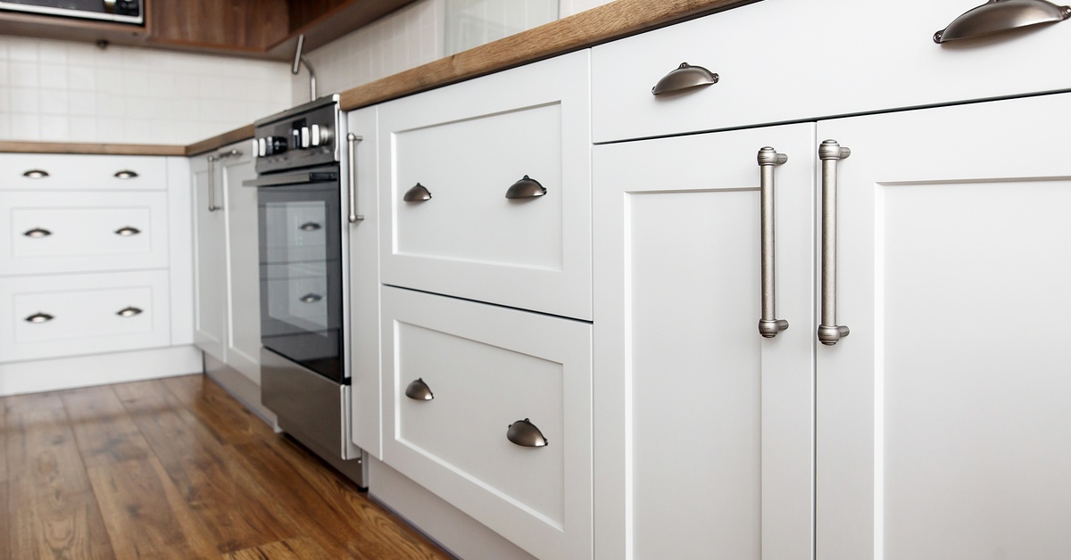 White kitchen cabinets with silver hardware and wooden countertops. The kitchen features an oven and a microwave.