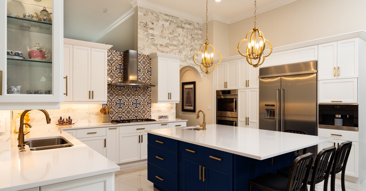 A luxurious open kitchen featuring navy and white two-toned cabinets and two golden chandeliers hanging above the island.
