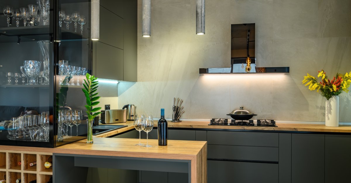 Modern kitchen with matte cabinets, wood countertops, glassware display, wine storage, pendant lighting, and fresh floral accents.